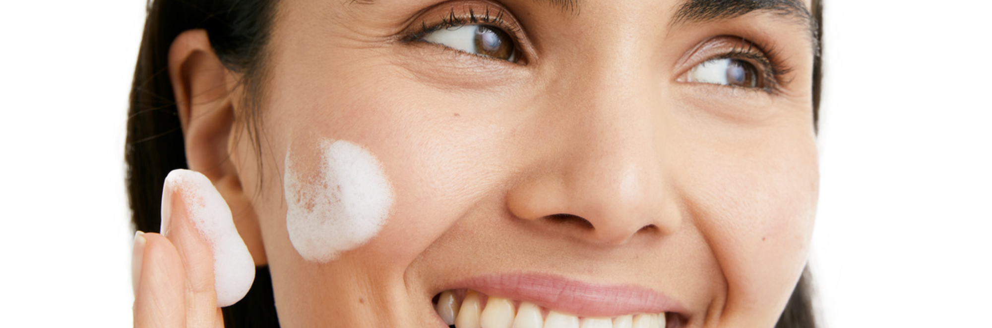 Woman smiling and applying face cream on a white background