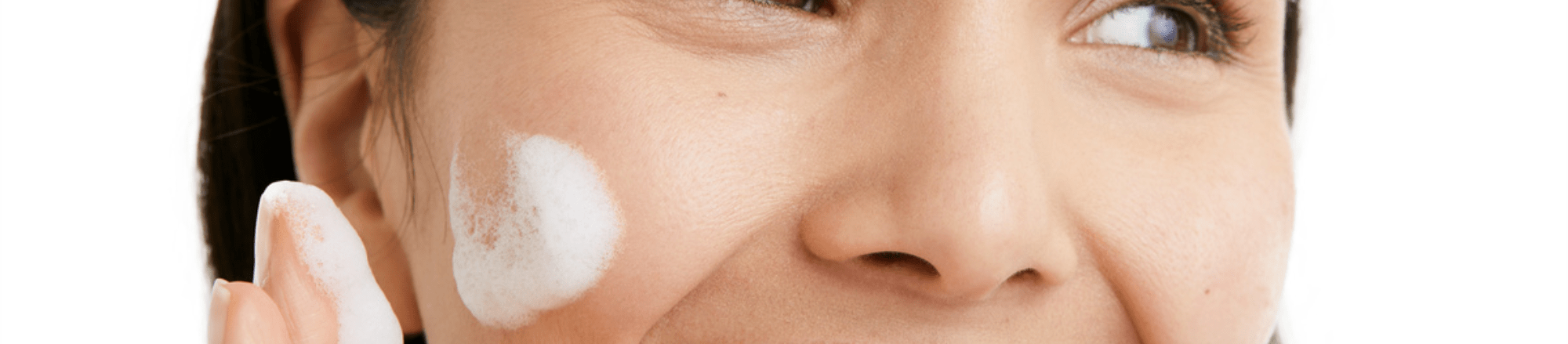 Woman smiling and applying face cream on a white background
