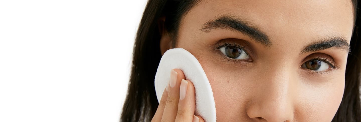 woman cleansing her skin with a cotton pad