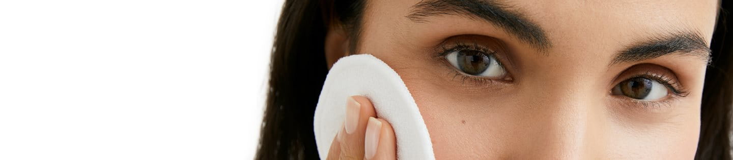 woman cleansing her skin with a cotton pad