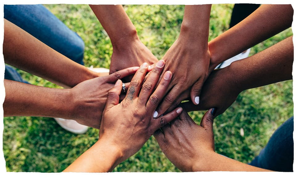Ludzie łączą ręce w kręgu, co symbolizuje pracę zespołową.