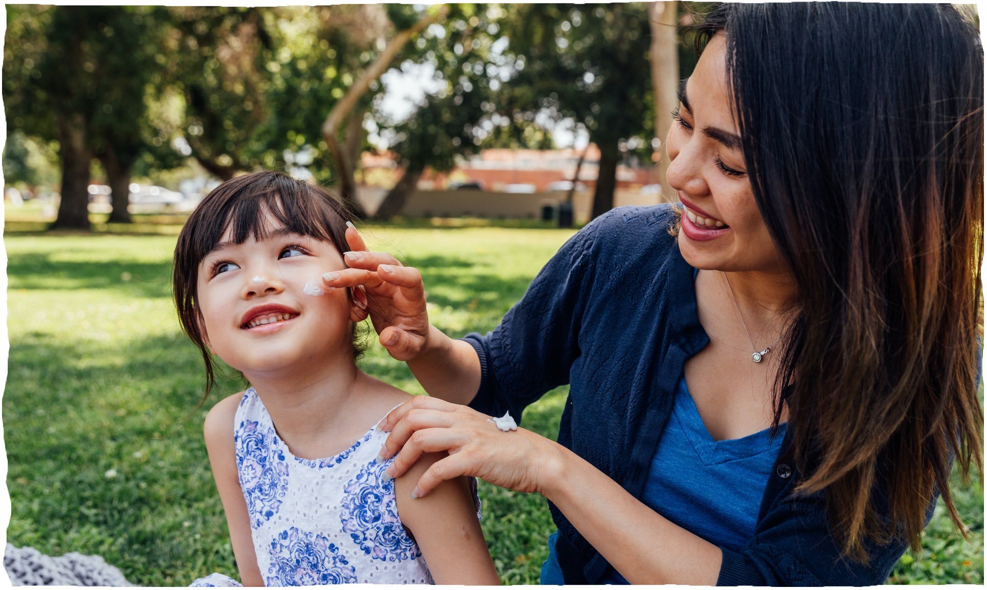 Eine Frau cremt Gesicht eines kleinen Kindes in Park ein.