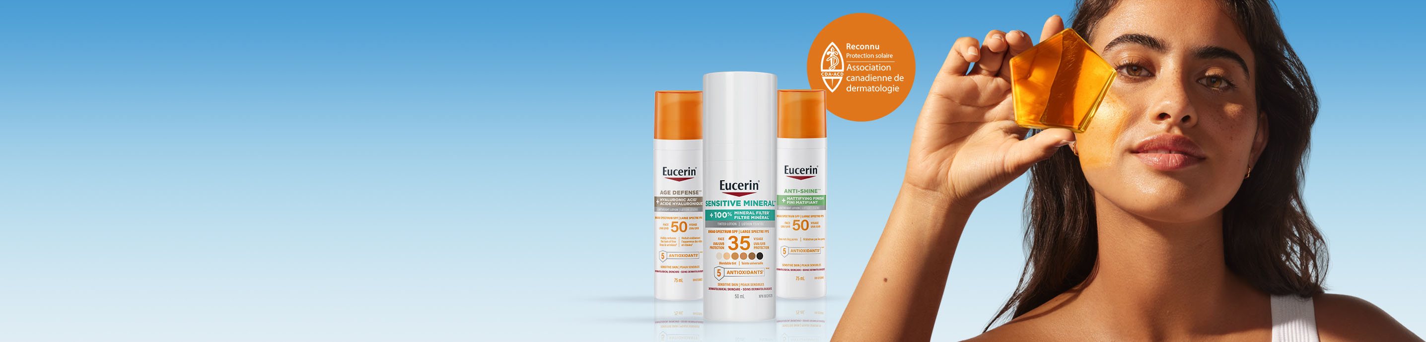 A person standing next to three Eucerin sunscreen products holding a piece of transparent orange material up to her eye.