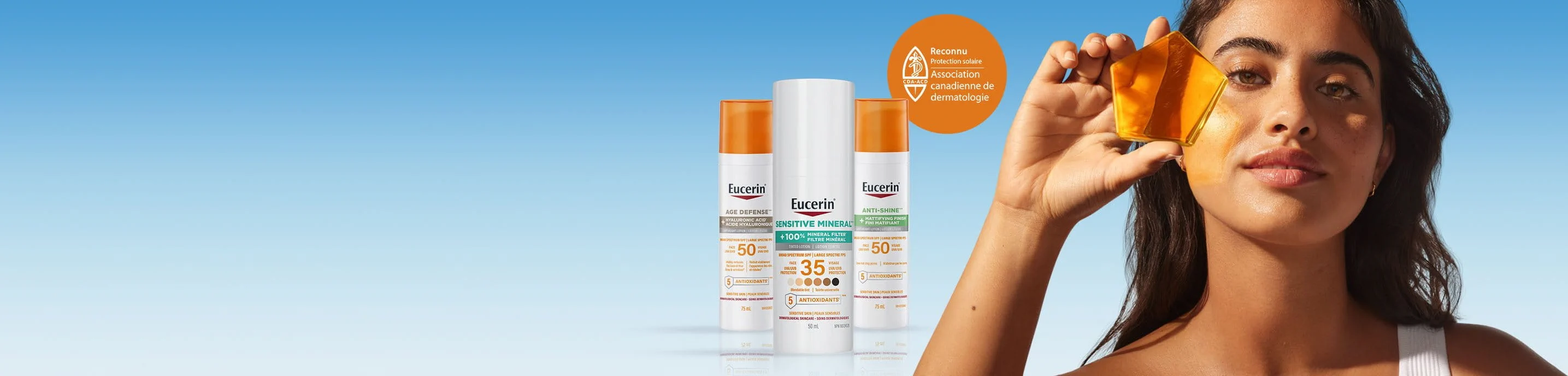 A person standing next to three Eucerin sunscreen products holding a piece of transparent orange material up to her eye.