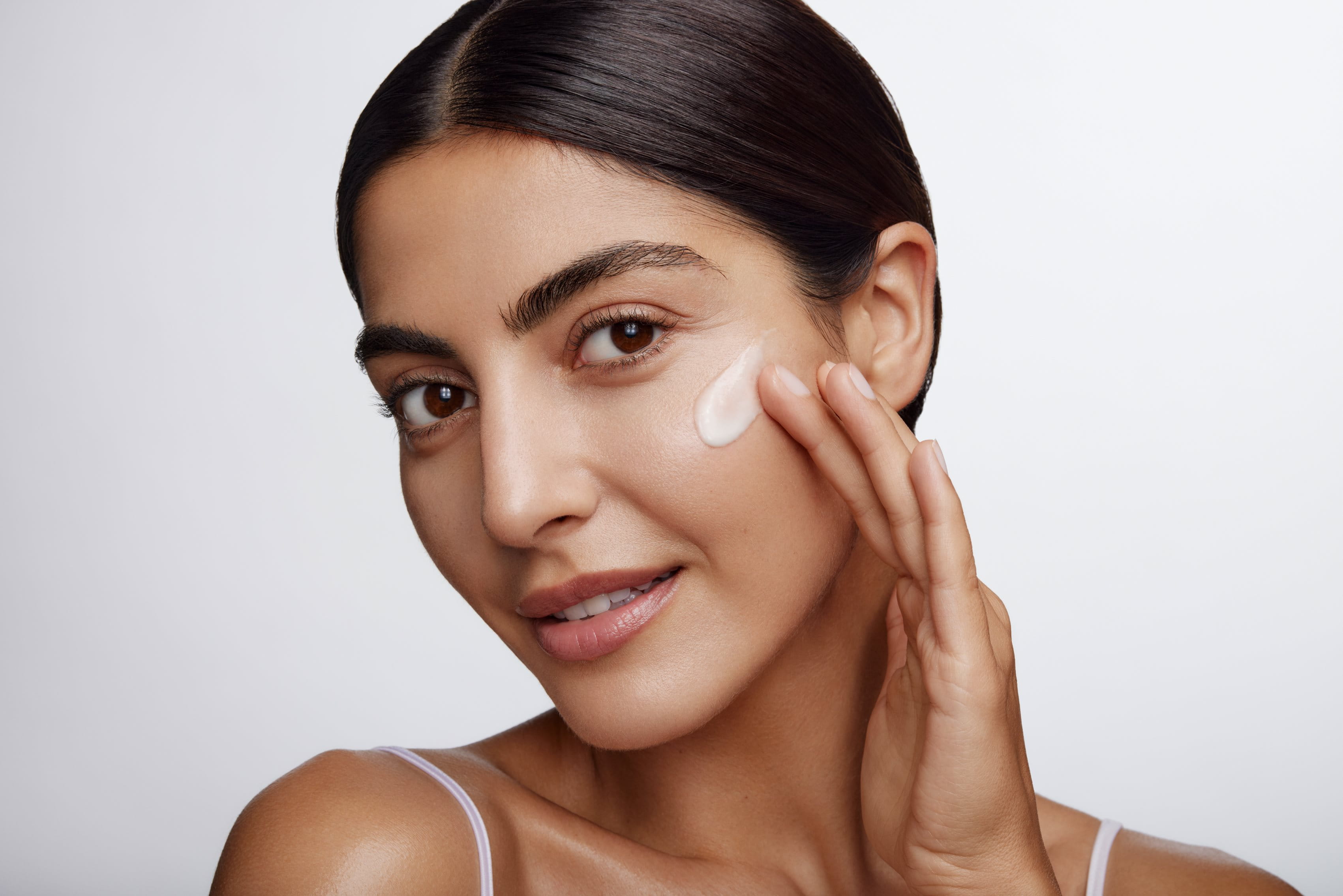 Woman applying a cream on her face on a grey background
