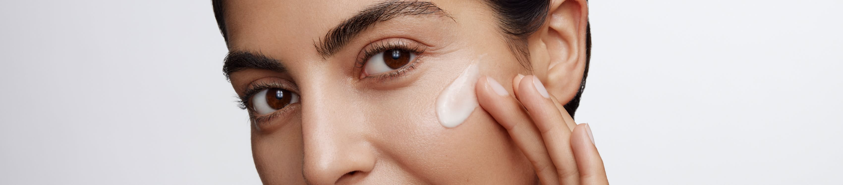Woman applying a cream on her face on a grey background