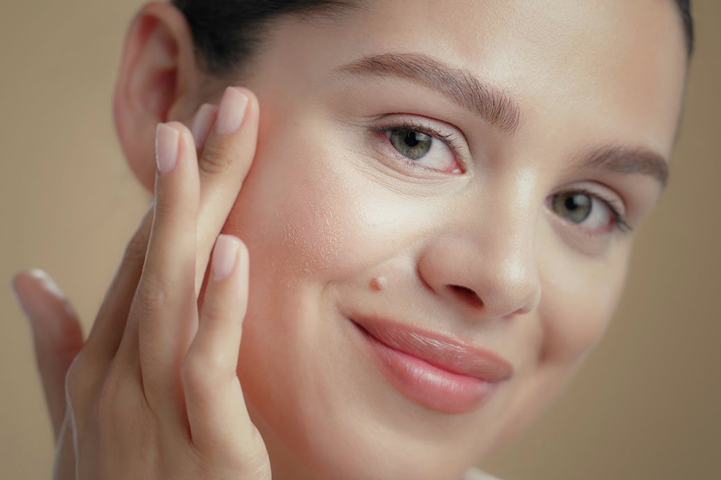 Donna dalla pelle luminosa applica un detergente oleoso sul viso come step della doppia detersione.