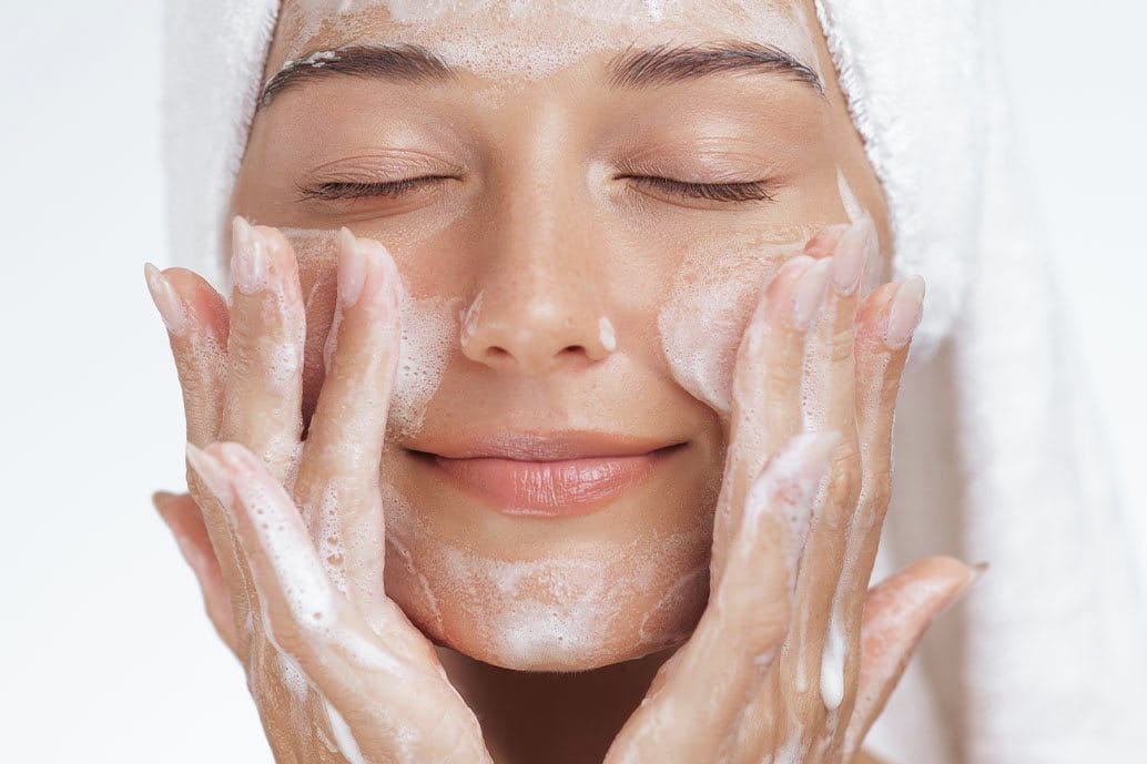 Donna che si deterge il viso con un detergente schiumogeno