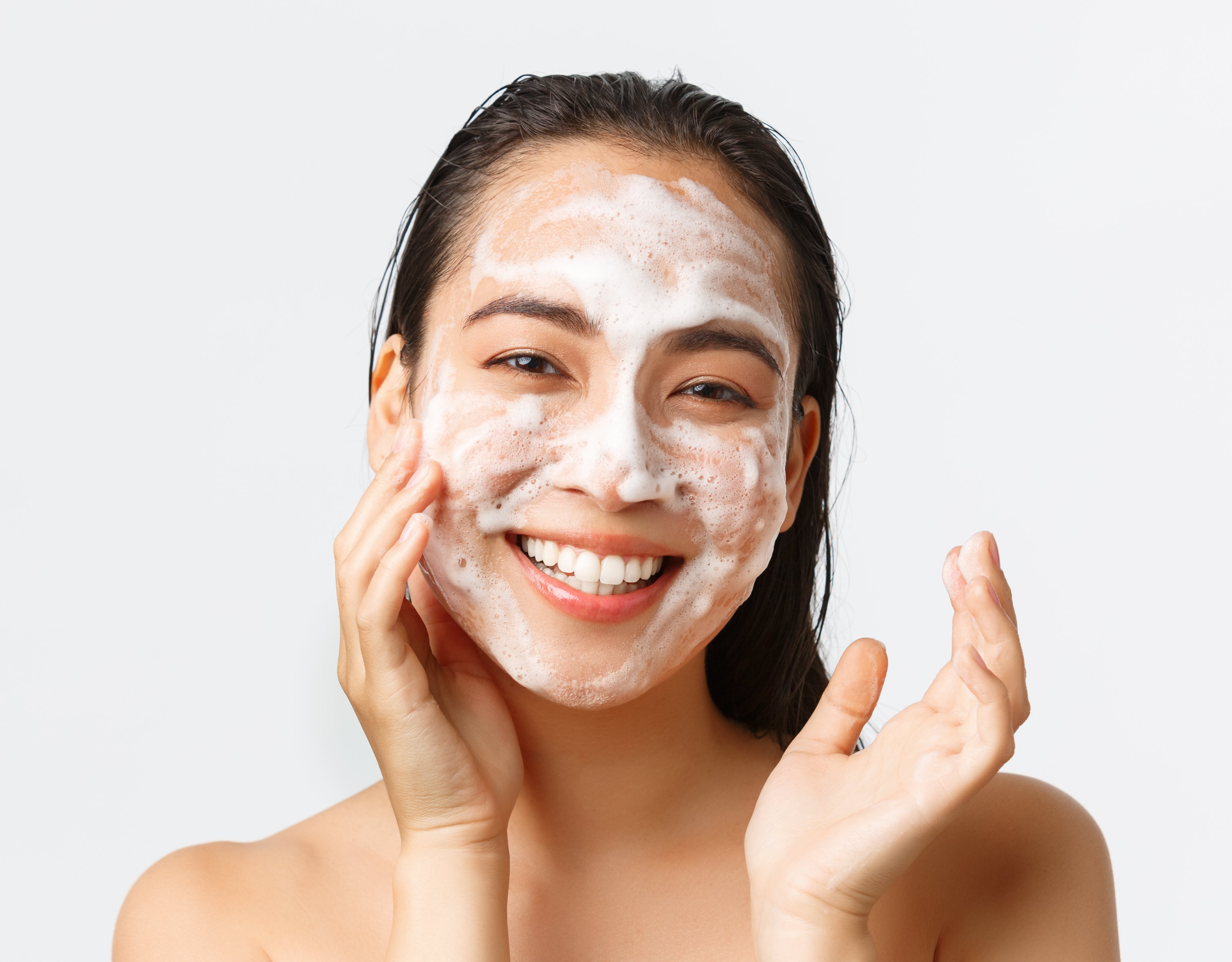 Eine Frau reibt sich lächelnd das Gesicht mit einem Reinigungsschaum ein.