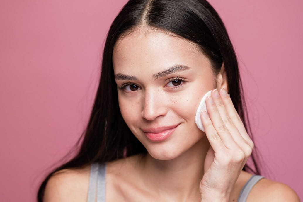Donna applica tonico sul viso con dischetto di cotone