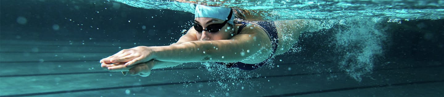 Nuotatrice sott'acqua in piscina mentre esegue una bracciata, indossando occhialini e cuffia