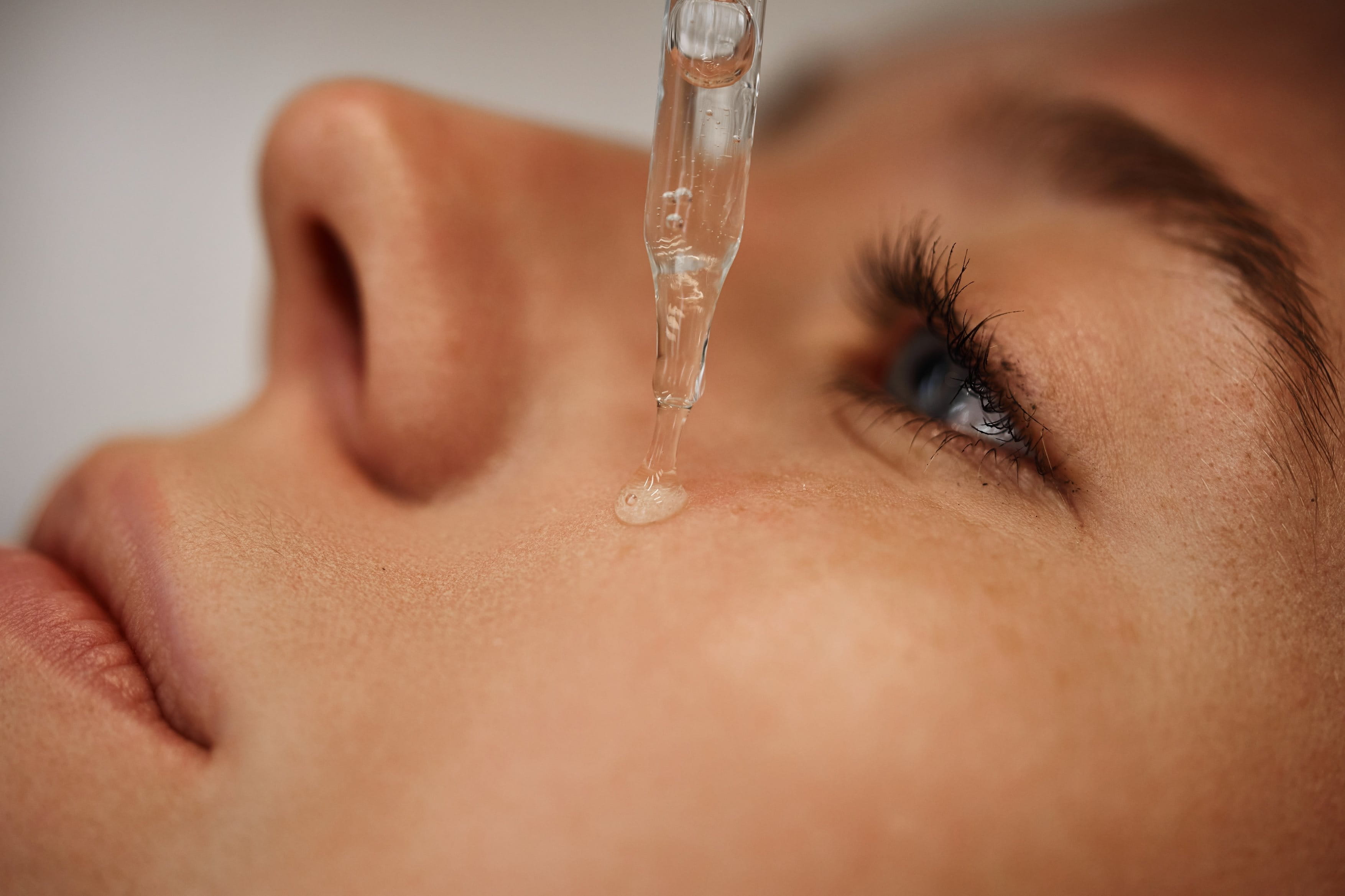 Eine lächelnde rothaarige Frau trägt mit einer Pipette ein Serum auf ihre Wange auf.