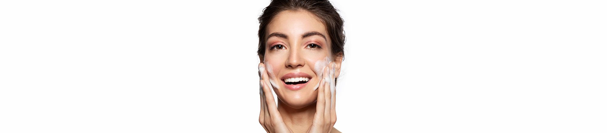 Ragazza sorride mentre massaggia il viso con un detergente schiumoso durante la doppia detersione quotidiana.