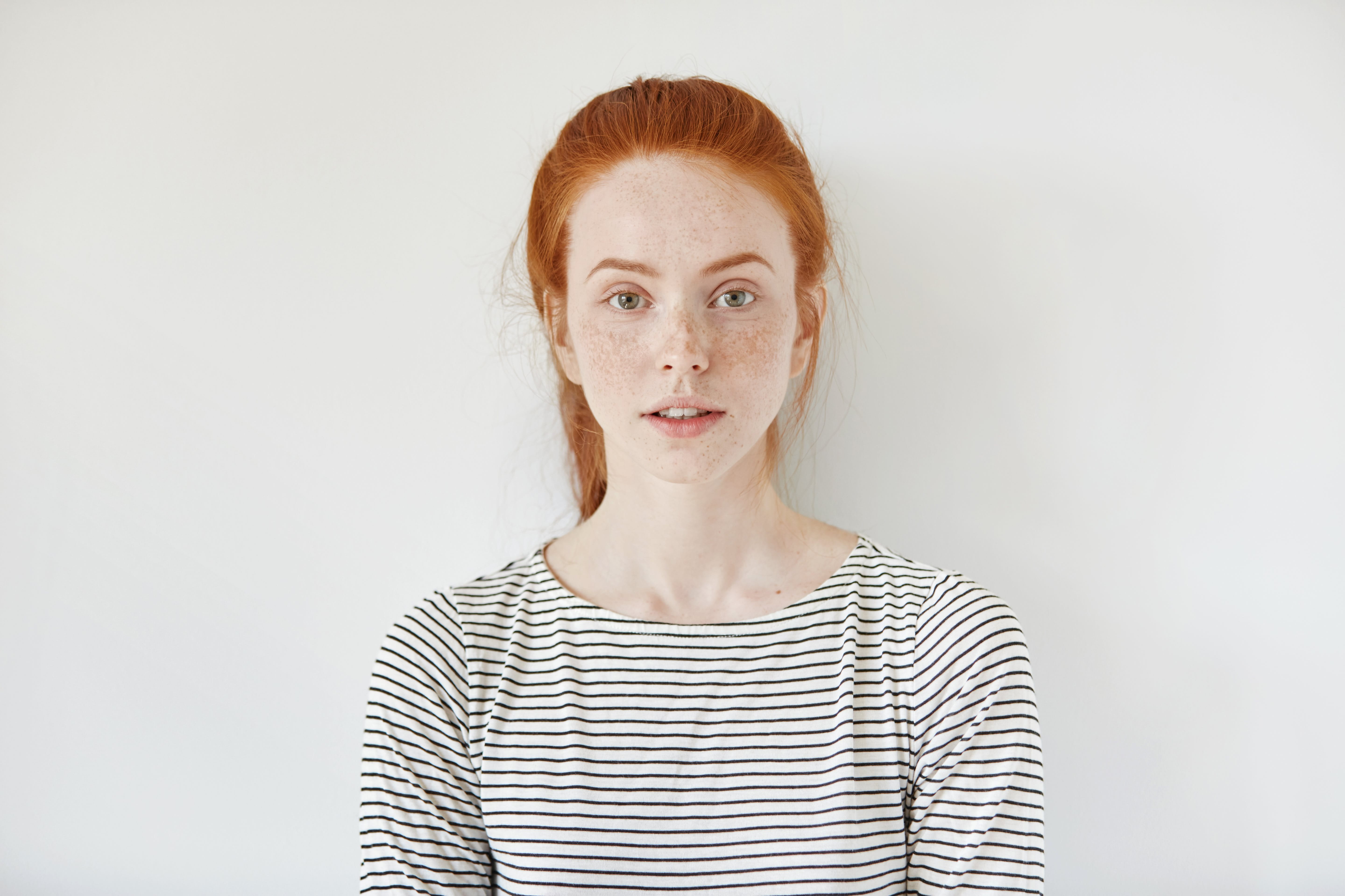 Portrait einer hellhäutigen jungen Frau mit roten Haaren, die Sommersprossen auf Nase und Wangen hat