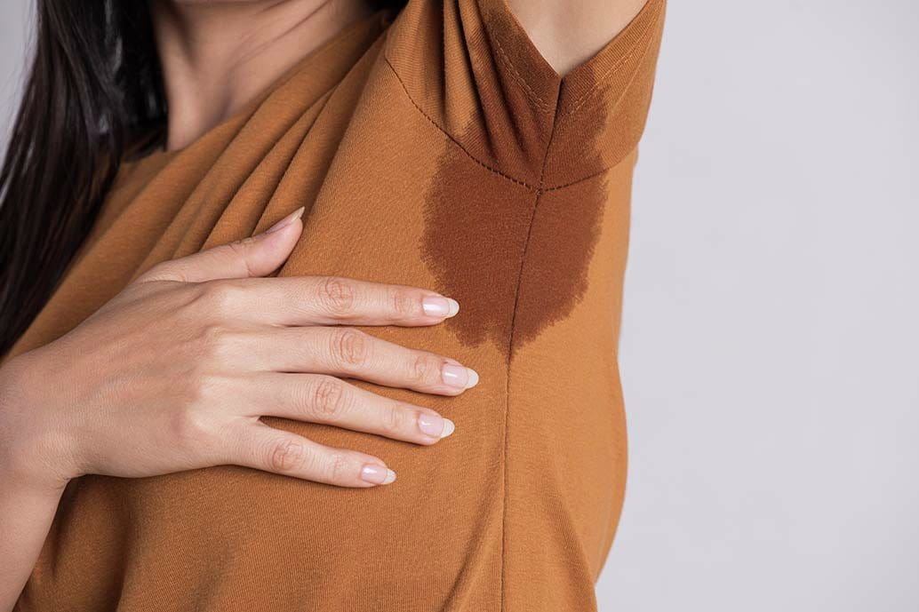 Foto di donna con maglietta aderente e braccio alzato con macchia di sudore nella zona ascellare