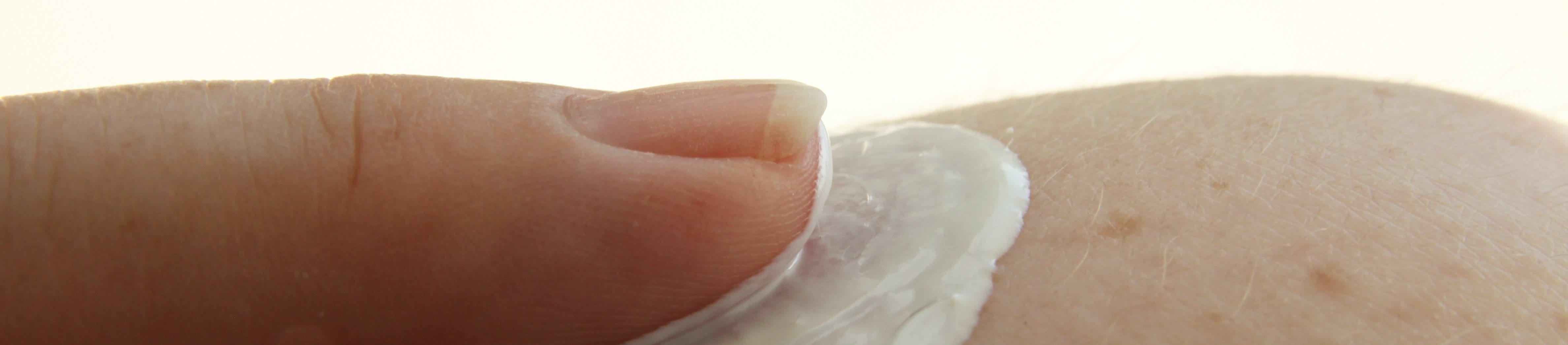 Ein Finger trägt weiße Sonnencreme punktuell auf die Haut auf.