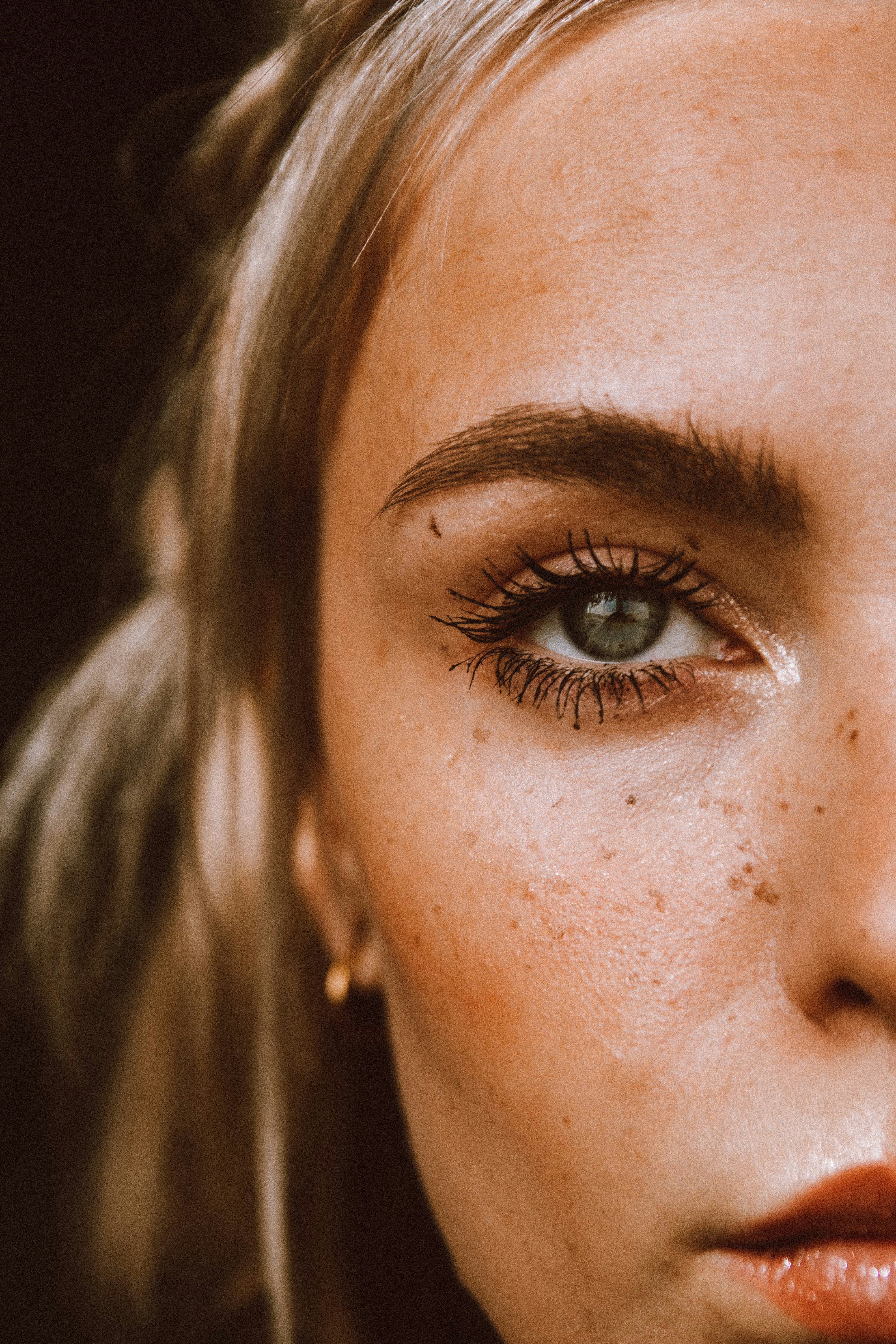 Nahaufnahme der linken Gesichtshälfte einer jungen kaukasischen Frau mit kleinen Pigmentflecken im Bereich der Augenpartie