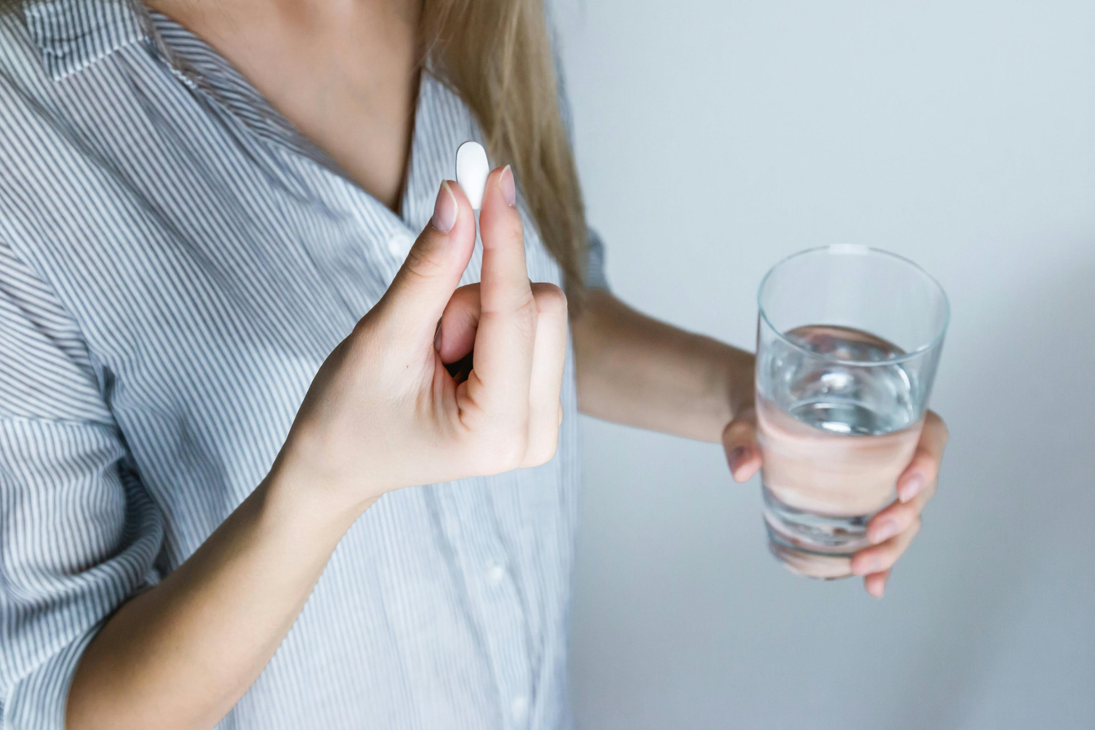 Eine Person hält eine weiße Tablette in der Hand und ein Glas Wasser in der anderen. Manche Medikamente können als Nebenwirkung einen Flush auslösen.