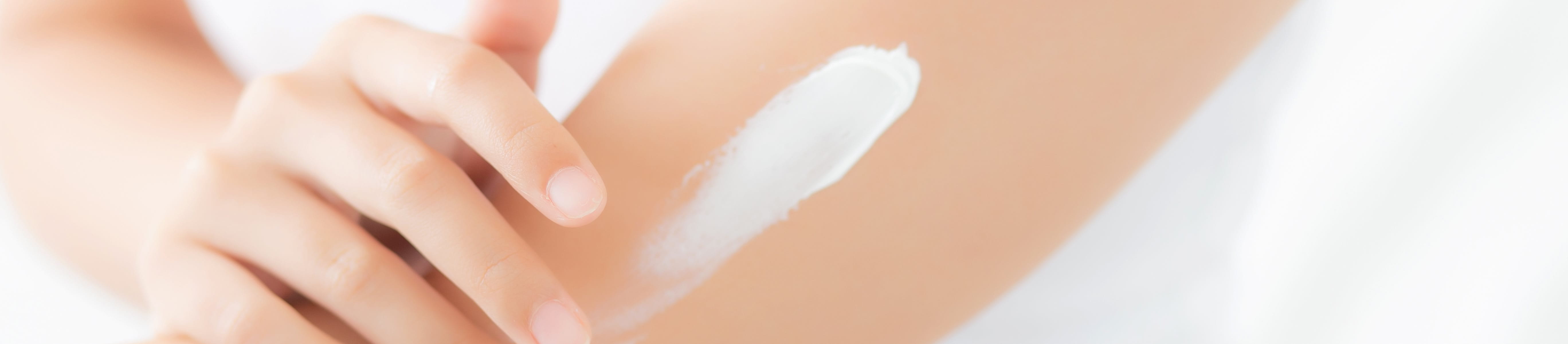 Nahaufnahme des Oberkörpers einer Frau mit ausgestrecktem Arm, die weiße Creme auf ihren Oberarm aufträgt