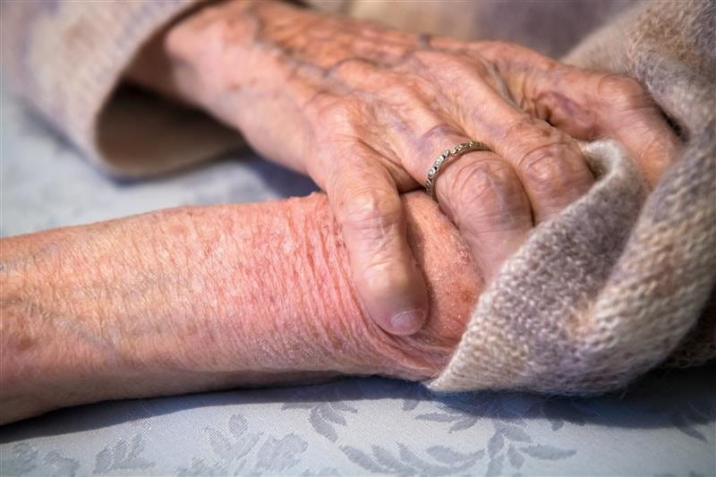 Eine Hand liegt auf einem Unterarm. Die Haut ist sehr dünn, trocken und Blutgefässe scheinen durch.