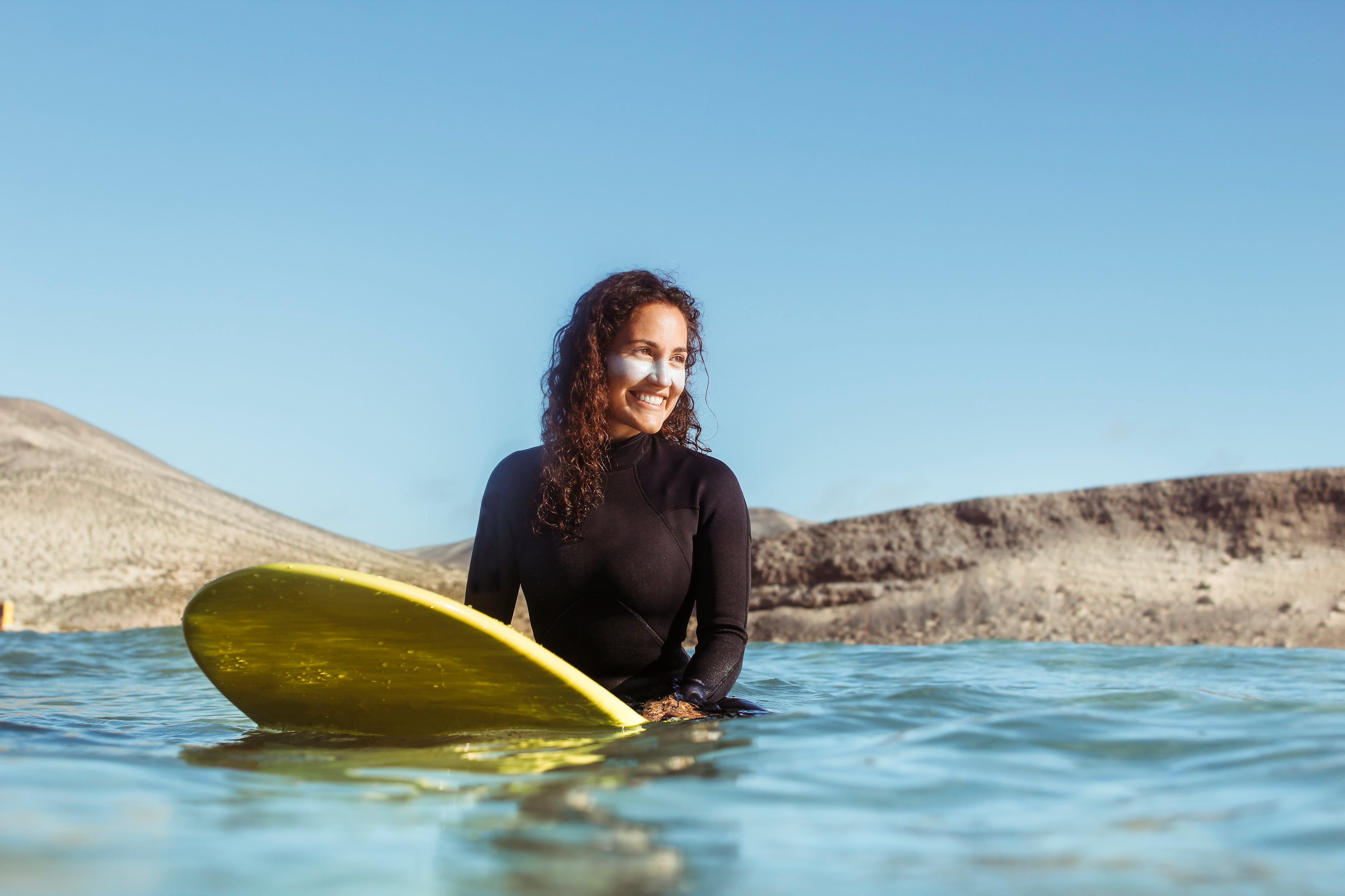 Junge Frau schützt sich mit Neoprenanzug und Sonnencreme beim Surfen.