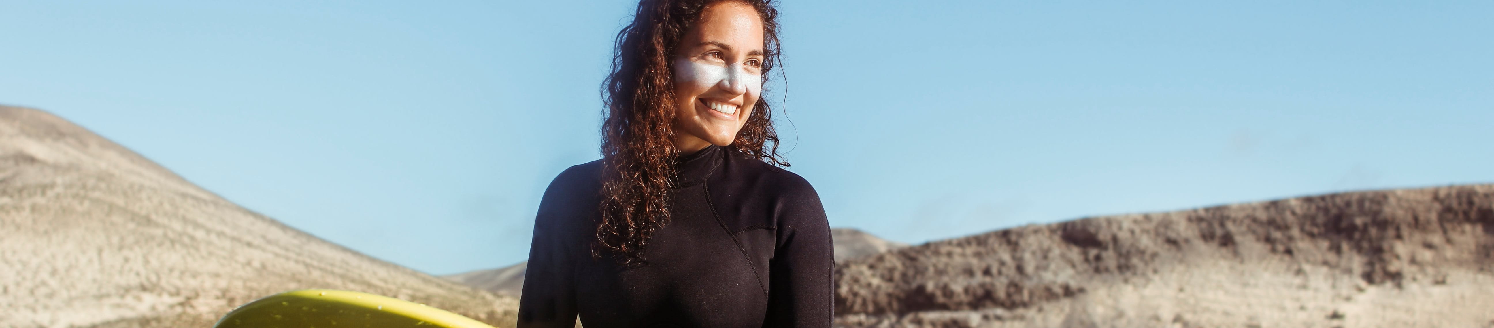 Junge Frau schützt sich mit Neoprenanzug und Sonnencreme beim Surfen.