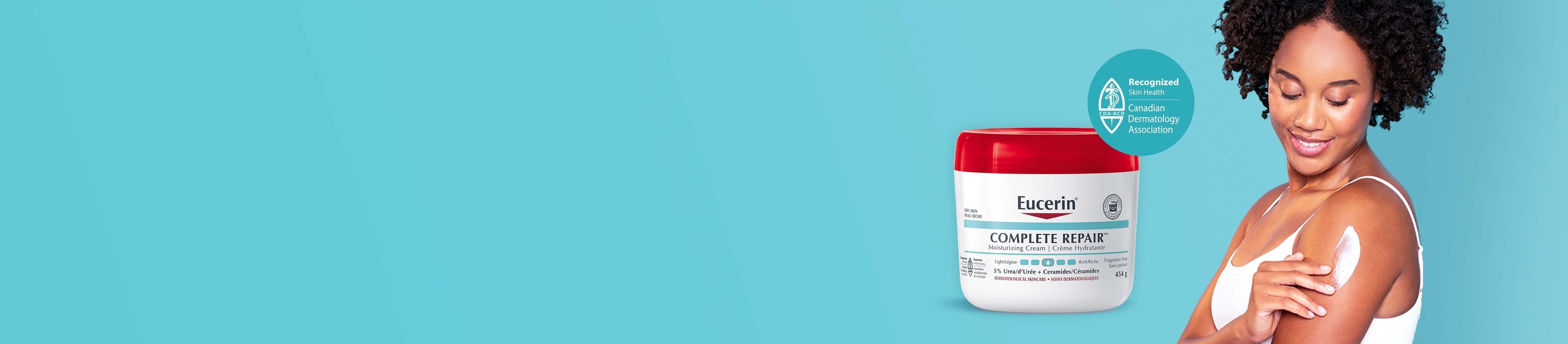 View of a female model wearing a white tank top and sitting down with her knees bent with the Eucerin Complete Repair 454g product in the background.