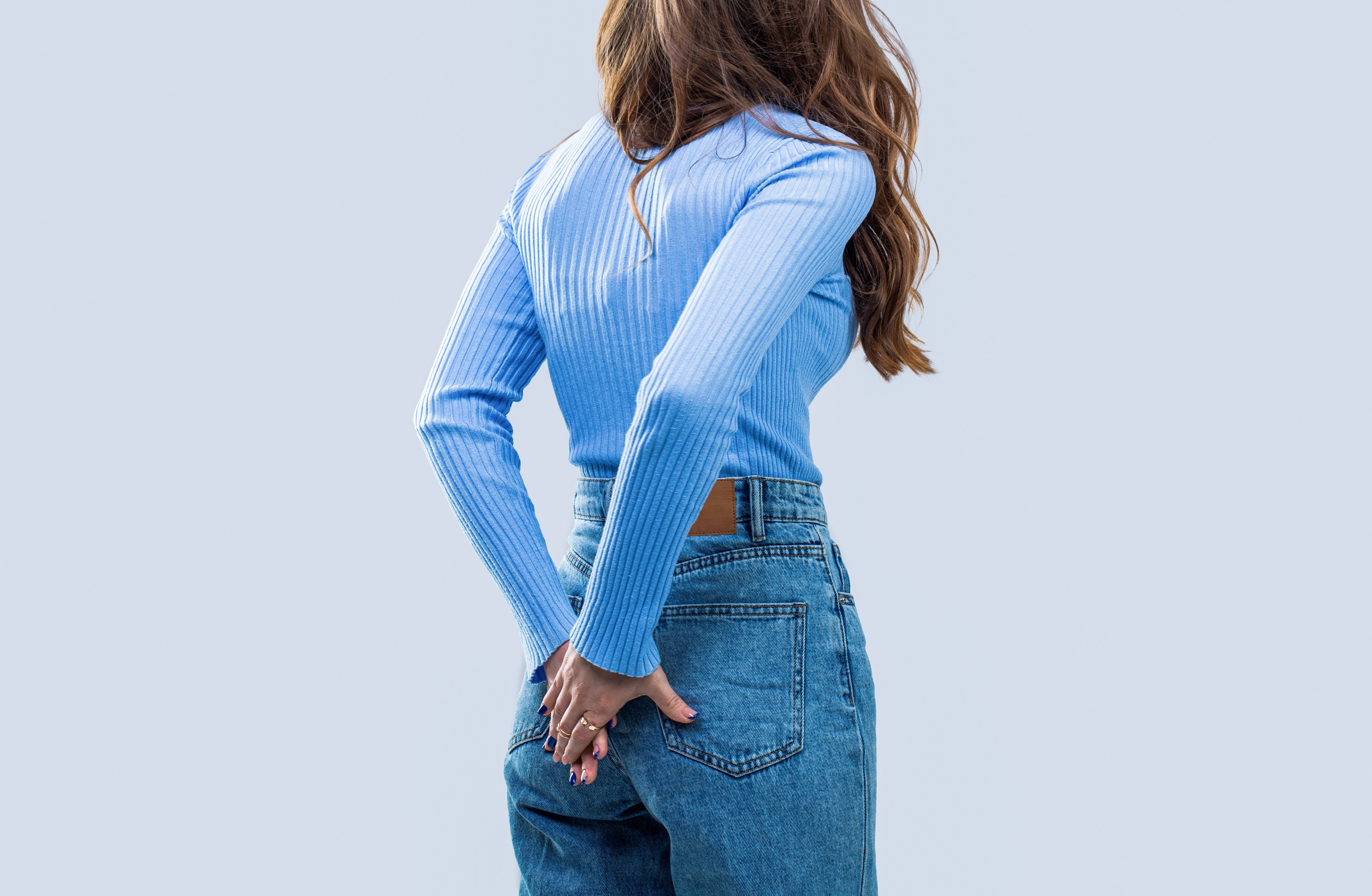 Eine Frau in blauer Jeans und hellblauem Oberteil steht mit dem Rücken zur Kamera und hält sich beide Hände vor den Hintern.