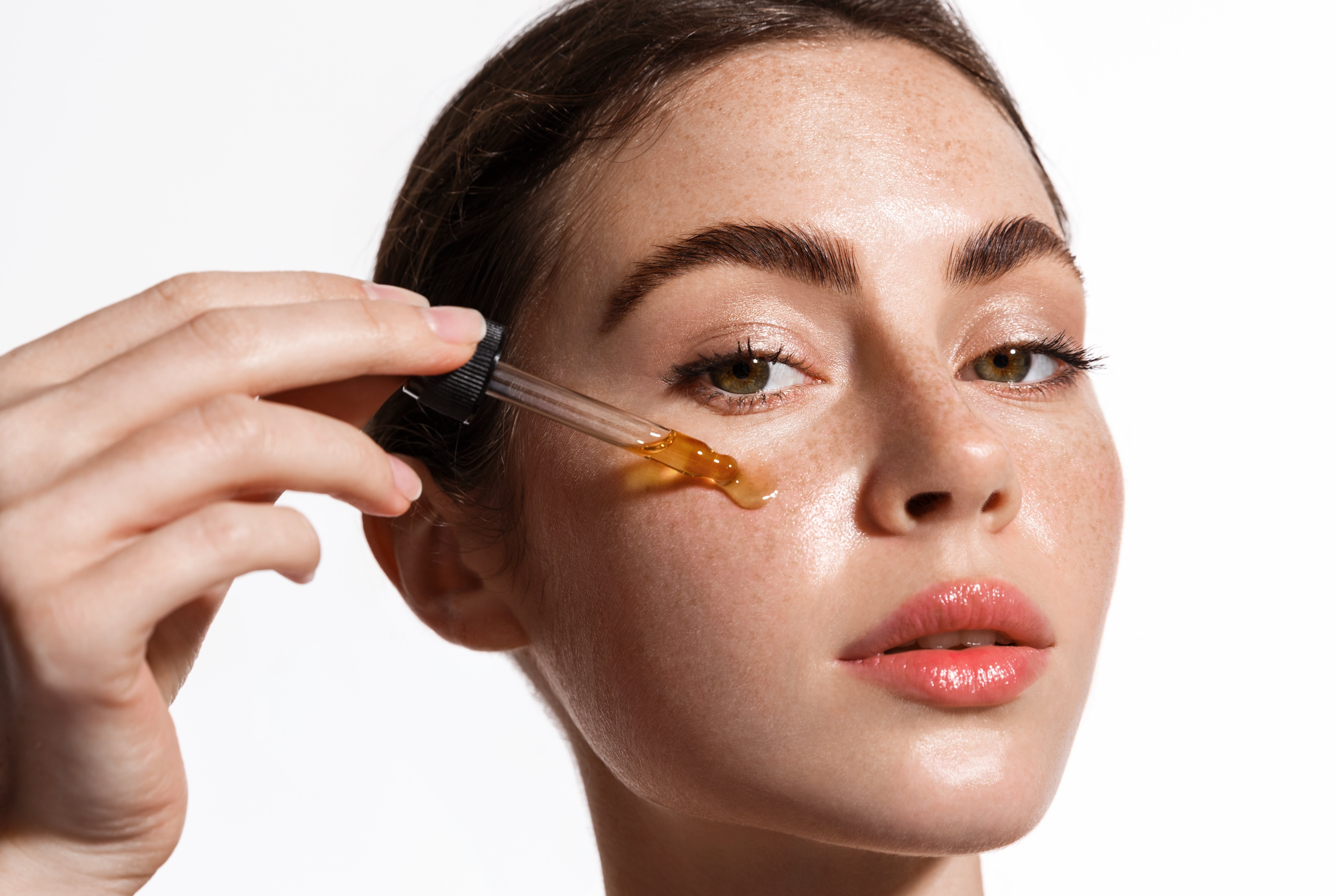Eine Frau trägt ein Öl mit einer Pipette auf ihre Wange auf.