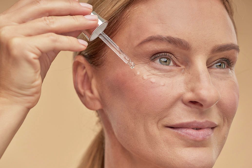 Donna sorride mentre applica siero viso sulla pelle