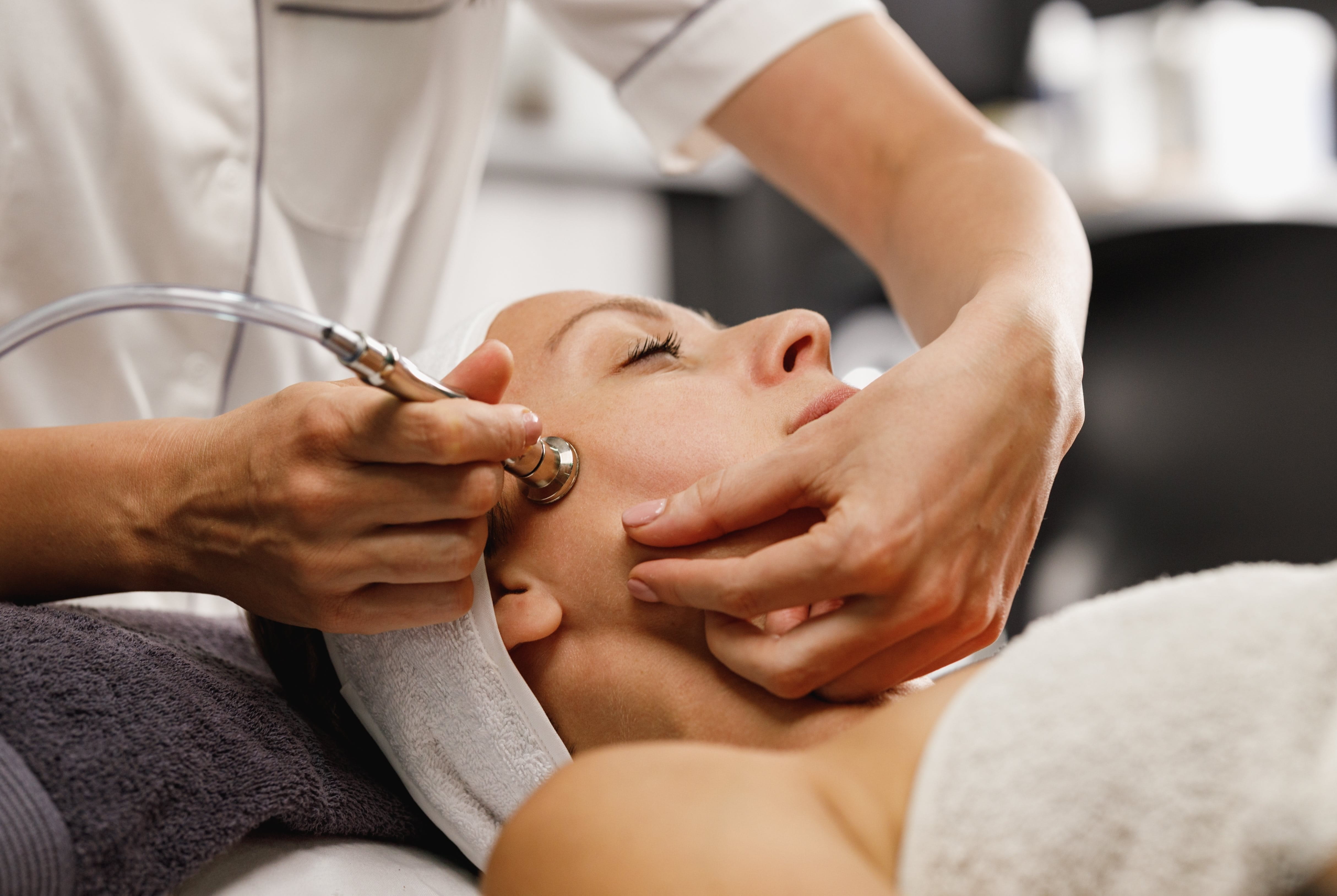 Eine Frau erhält eine Microdermabrasion-Behandlung im Kosmetikstudio, Nahaufnahme des Gesichts mit einem Hautpflegegerät.