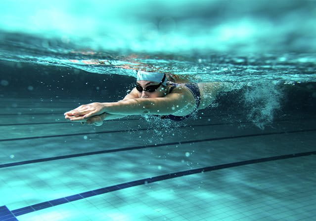 Nuotatrice sott'acqua in piscina mentre esegue una bracciata, indossando occhialini e cuffia