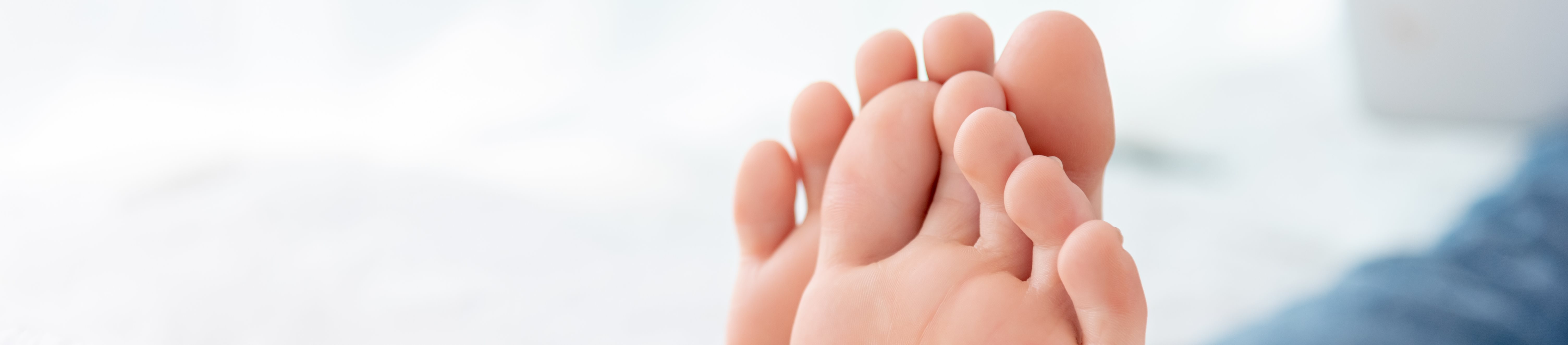 Nahaufnahme der Füße einer Frau in Jeans auf weißer Bettwäsche.