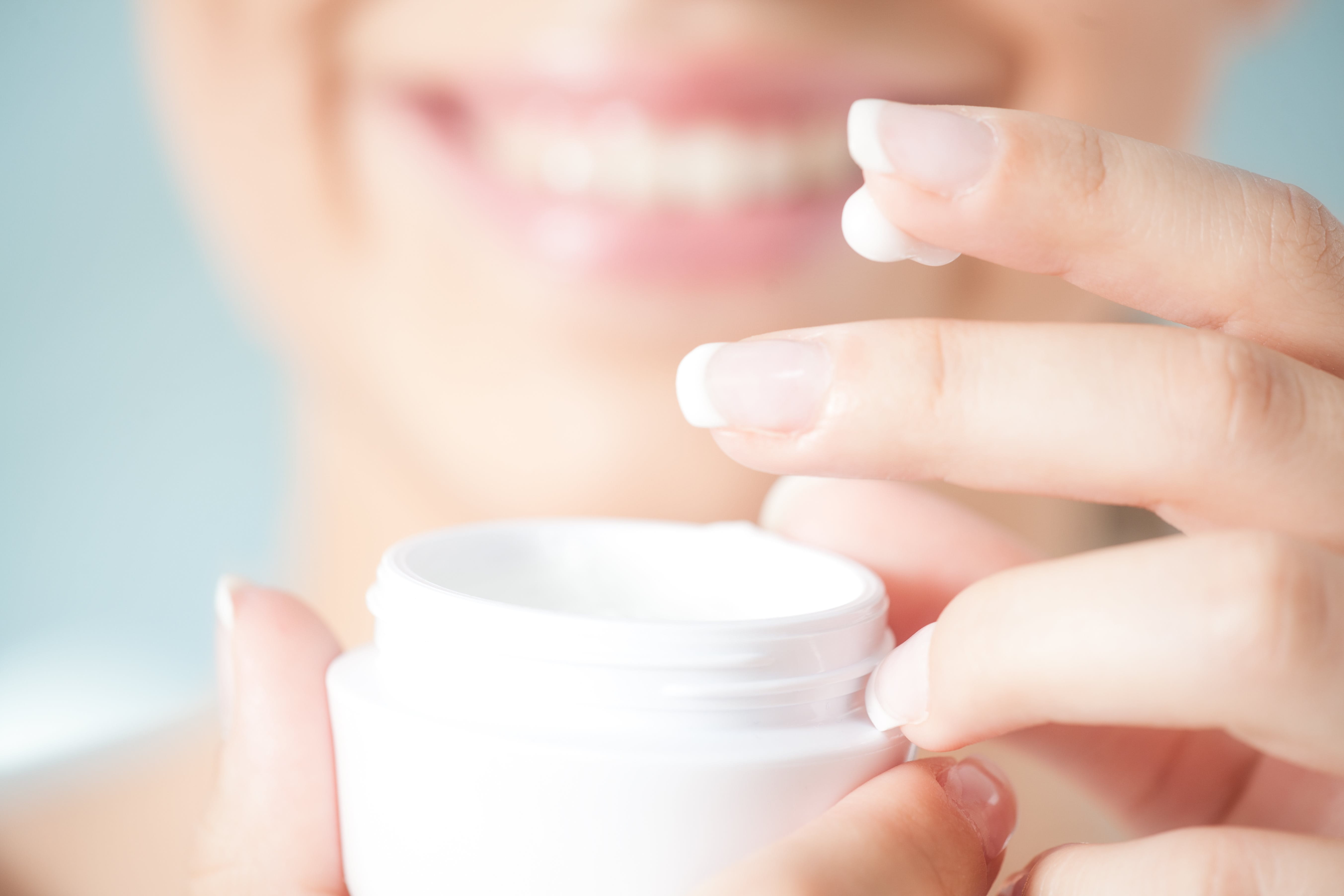 Frau hält eine Dose mit Creme in der Hand und hat Creme an den Fingern.