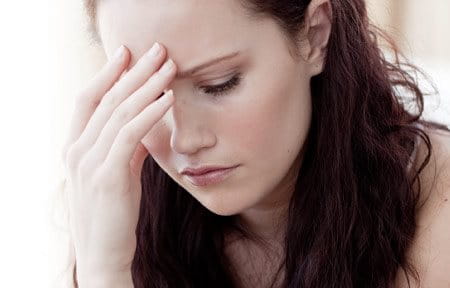 Eine Frau mit schmerzvollem Gesichtsausdruck berührt mit ihrer rechten Hand die Stirn. 