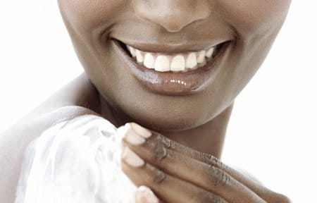 Woman with dark skin is applying sunscreen on her right shoulder