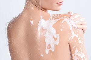 Woman applying moisturizer to her back in the shower