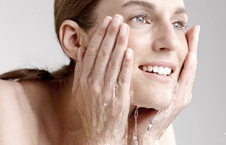 Eine Frau schöpft sich mit beiden Händen Wasser ins Gesicht und reinigt so ihre Haut. 