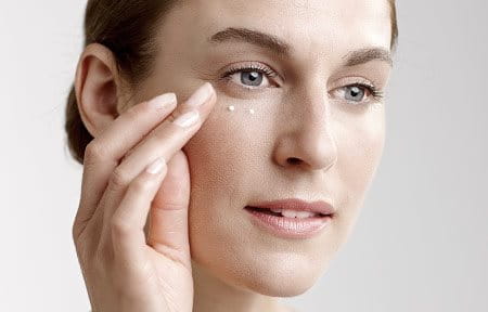 Woman applies eye cream.