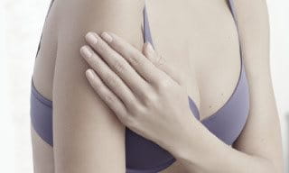 Woman wearing a bra, touching her left arm.