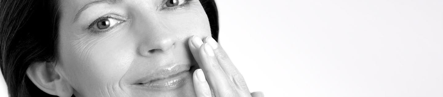 Middle-aged woman touching left cheek with hand.
