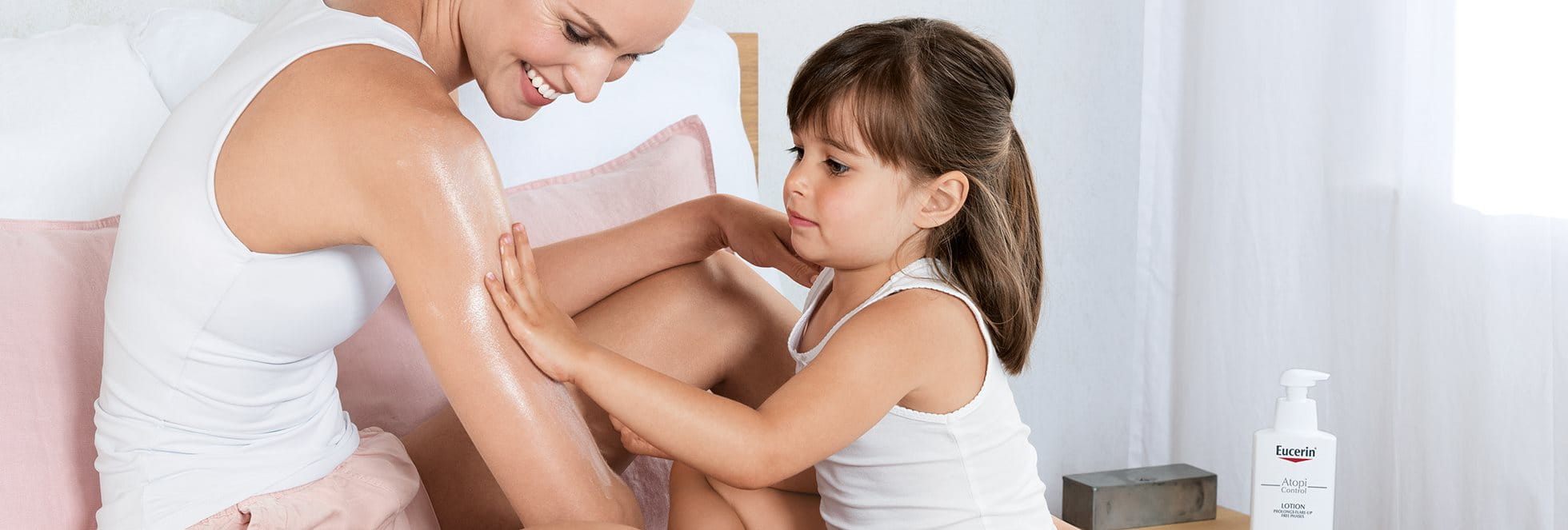 A mother and her daughter. The girl is using the Eucerin Atopi comfort creme on her mother's arm.