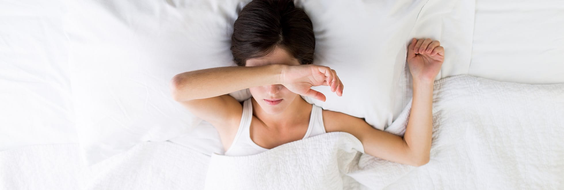Woman laying in bed covering her face with her hand