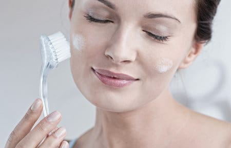 woman exfoliating her face with a dry brush
