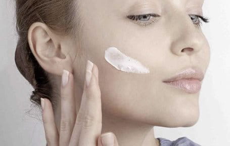 Woman applying cream on her cheek