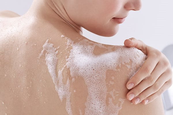 woman rubbing soap foam on shoulders