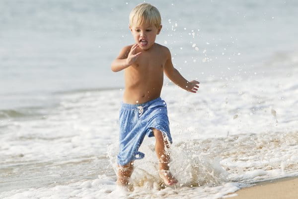 Barn som springer i vattenbrynet med extra vattenresistent solskydd