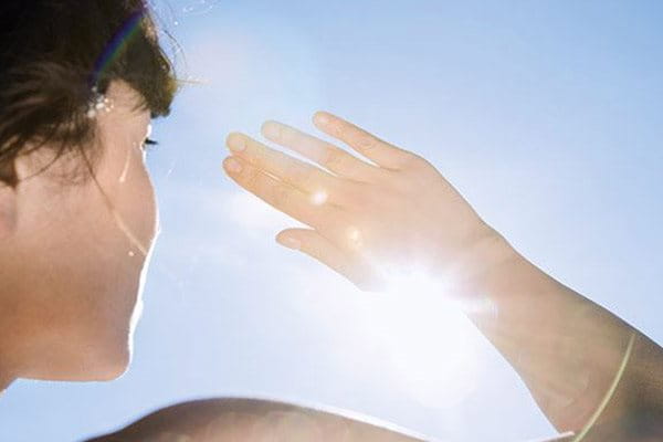 Frau schützt Gesicht mit der Hand vor der Sonne