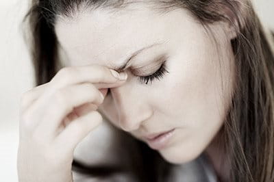 Eine junge Frau mit geschlossenen Augen und gestresstem Gesichtsausdruck, die sich mit zwei Fingern an die Nasenwurzel fasst.