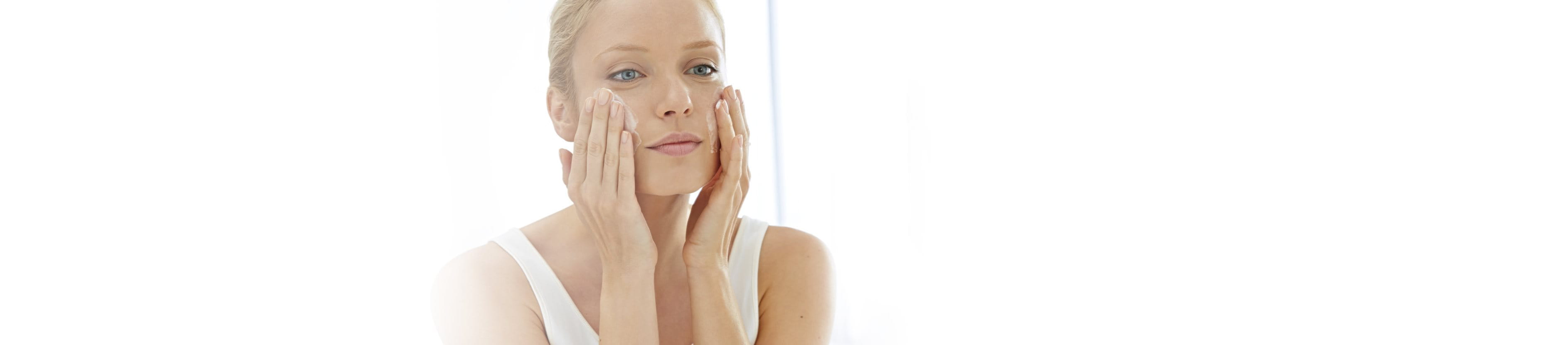 Junge blonde Frau cremt sich das Gesicht ein